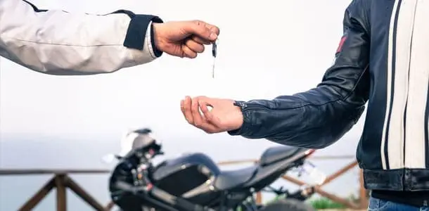 Person handing over motorbike key with motorcycle in background – secured motorbike loan approval Australia-wide.