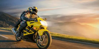 Two riders on a yellow sports bike travelling along a scenic Tasmanian road at sunset.